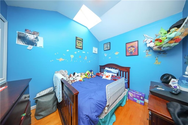 bedroom featuring vaulted ceiling with skylight, wood finished floors, and baseboards