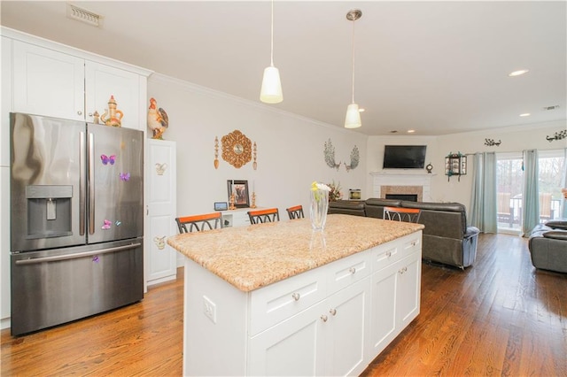 kitchen with visible vents, stainless steel fridge, open floor plan, a fireplace, and crown molding
