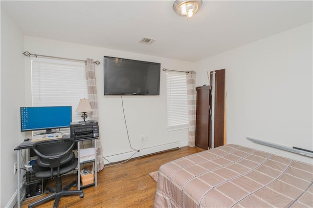 bedroom featuring visible vents, a baseboard heating unit, and wood finished floors