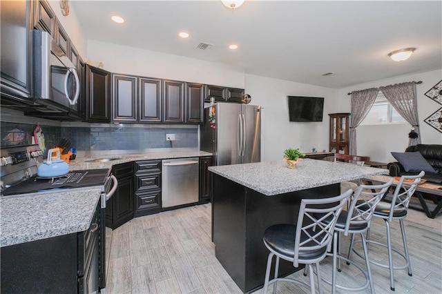 kitchen featuring tasteful backsplash, visible vents, appliances with stainless steel finishes, a kitchen island, and a breakfast bar area