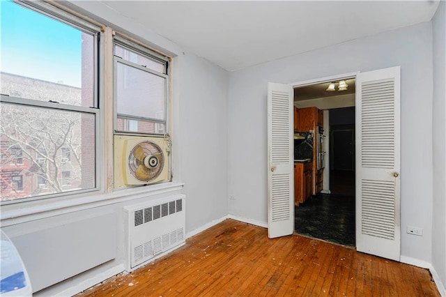empty room featuring radiator heating unit, wood-type flooring, plenty of natural light, and baseboards