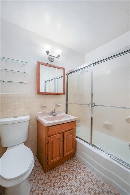 full bathroom featuring toilet, tile walls, bath / shower combo with glass door, and vanity