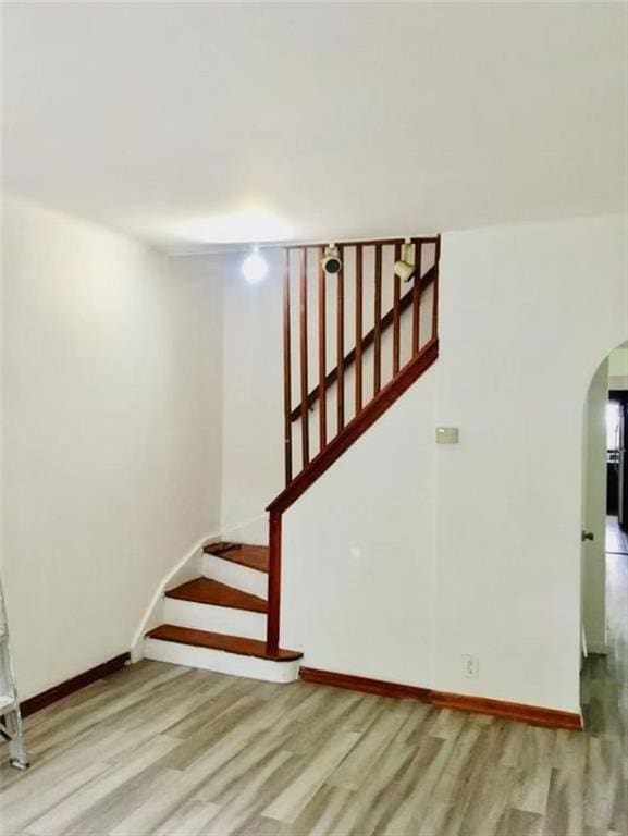 stairway with arched walkways, baseboards, and wood finished floors