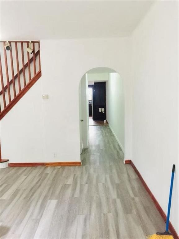 empty room featuring arched walkways, baseboards, wood finished floors, and stairway