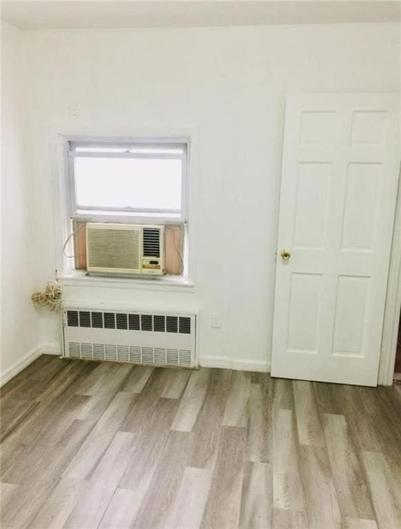 spare room with cooling unit, baseboards, radiator heating unit, and wood finished floors