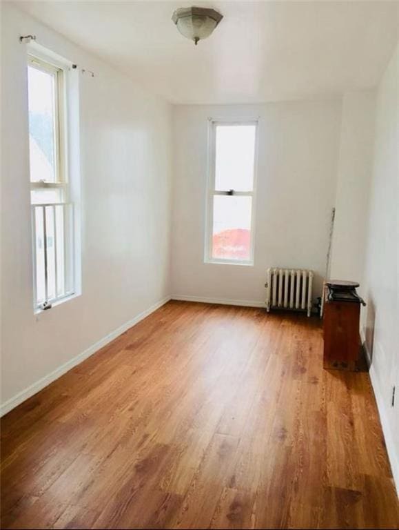 empty room with baseboards, radiator heating unit, and wood finished floors