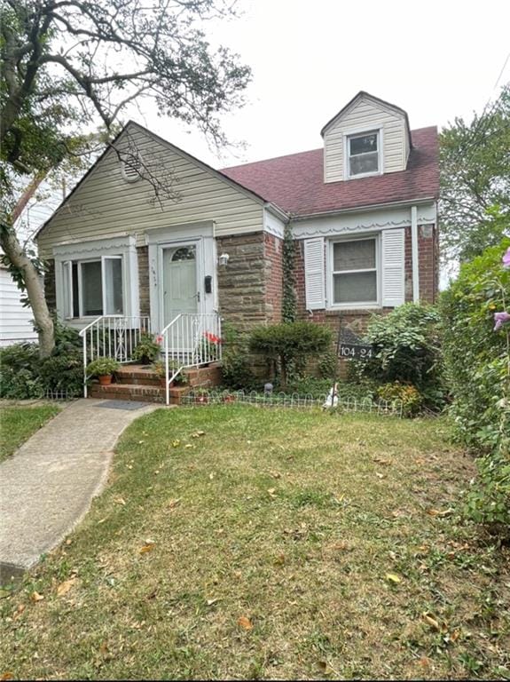 view of front facade featuring a shingled roof, brick siding, and a front yard