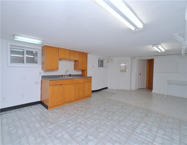 kitchen featuring a sink, light flooring, baseboards, and dark countertops