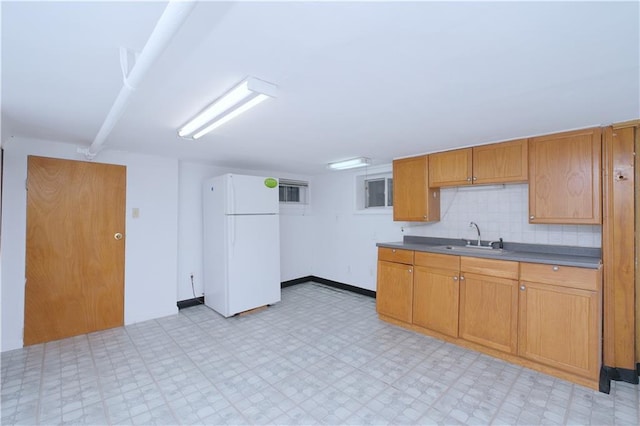 kitchen featuring freestanding refrigerator, light flooring, a sink, dark countertops, and brown cabinetry