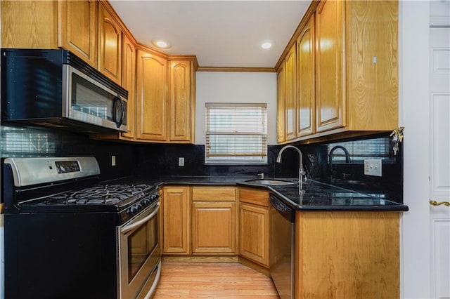 kitchen featuring stainless steel appliances, a sink, light wood-type flooring, decorative backsplash, and ornamental molding