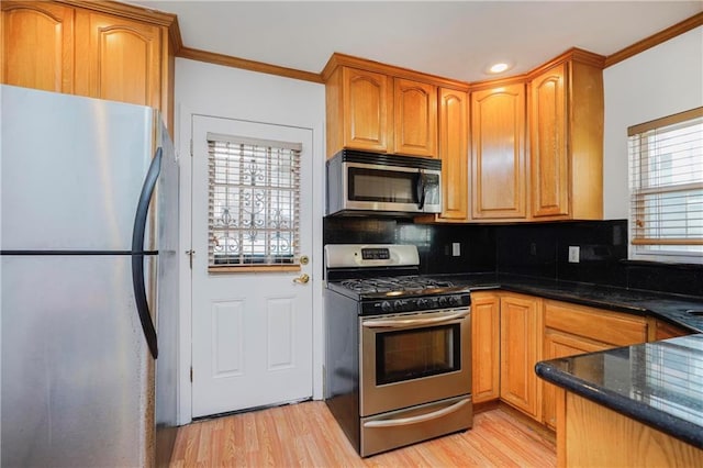 kitchen featuring appliances with stainless steel finishes, ornamental molding, decorative backsplash, light wood-type flooring, and dark stone counters