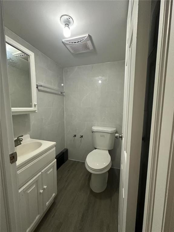 half bath featuring visible vents, tile walls, wood finished floors, vanity, and toilet