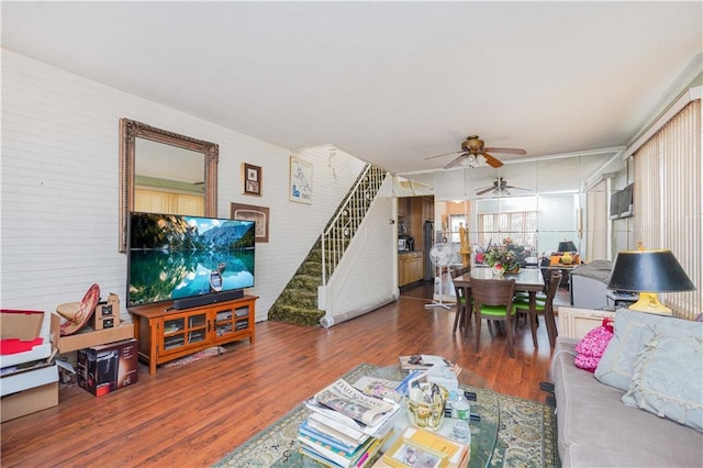 living area featuring brick wall, wood finished floors, stairs, and ceiling fan
