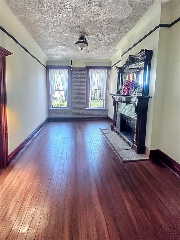 unfurnished living room with a fireplace, a textured ceiling, wood finished floors, and baseboards