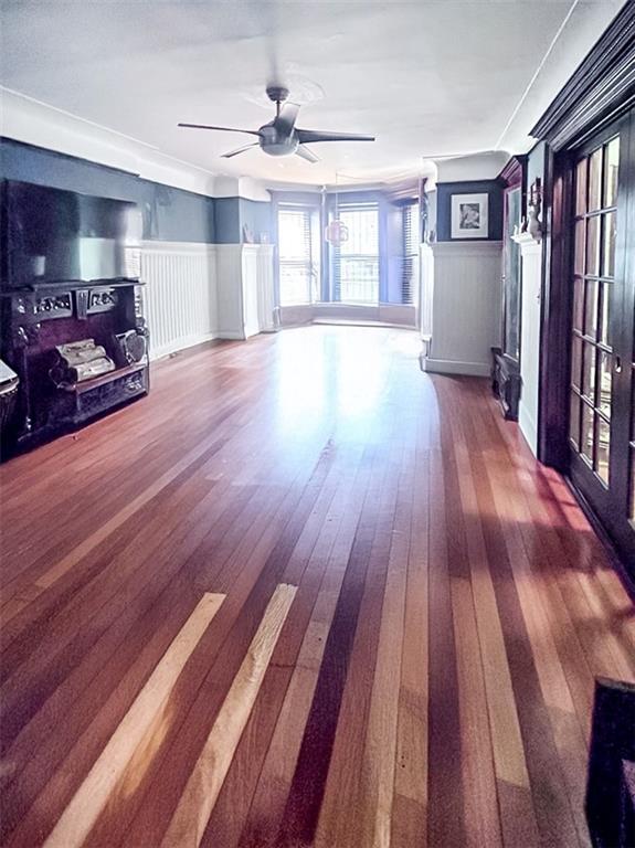 unfurnished living room with a wainscoted wall, ceiling fan, dark wood-style flooring, and a decorative wall
