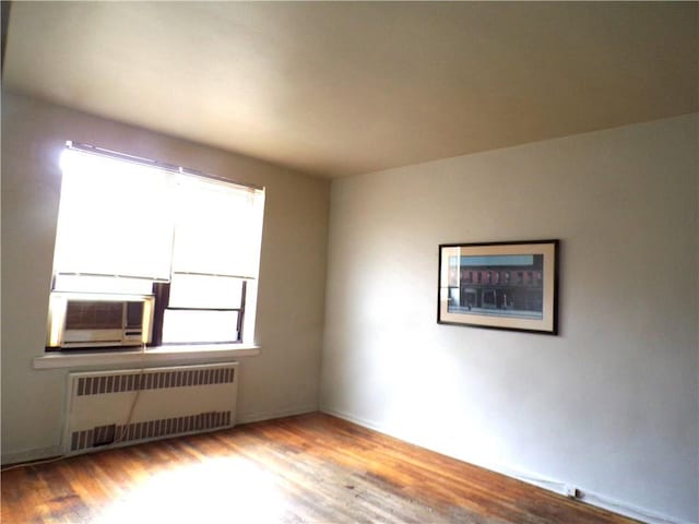 unfurnished room featuring cooling unit, radiator, and wood finished floors