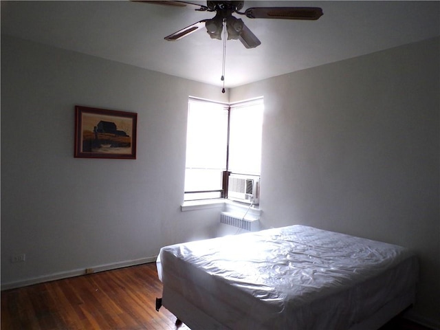bedroom with radiator, cooling unit, a ceiling fan, wood finished floors, and baseboards