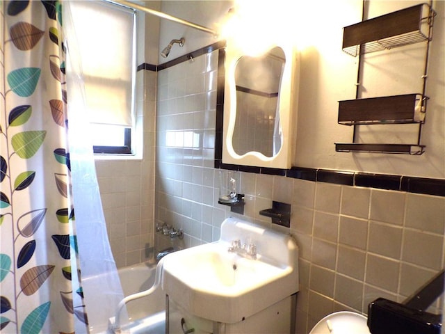 bathroom with shower / bath combination with curtain, toilet, a sink, and tile walls