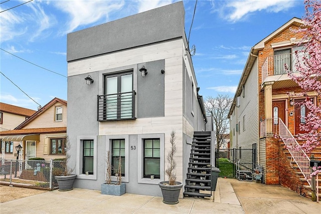 rear view of house with fence, stucco siding, and stairway