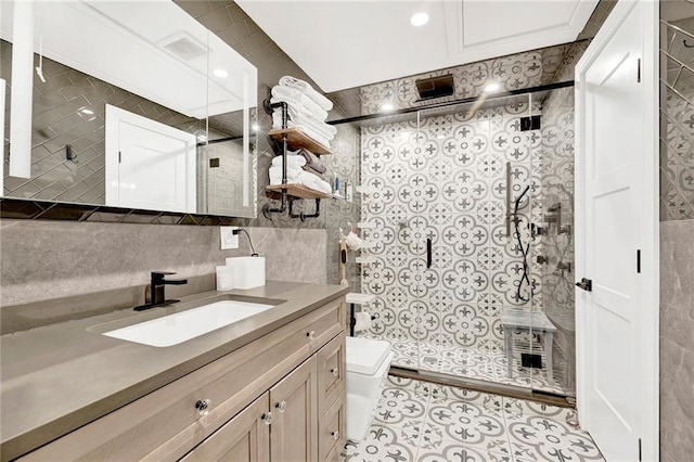 full bath with vanity, toilet, tiled shower, and tile walls