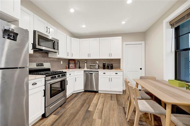 kitchen featuring light countertops, white cabinetry, a sink, light wood finished floors, and stainless steel appliances