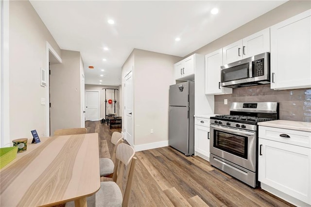 kitchen featuring backsplash, appliances with stainless steel finishes, wood finished floors, light countertops, and white cabinets