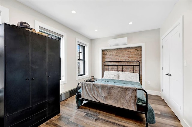 bedroom featuring baseboards, a wall unit AC, recessed lighting, and wood finished floors