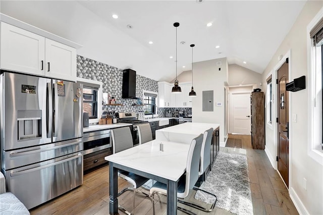 kitchen featuring wall chimney range hood, vaulted ceiling, white cabinets, stainless steel appliances, and light wood-style flooring