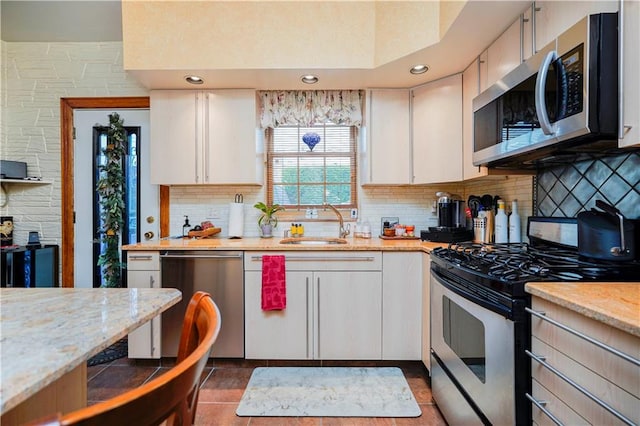 kitchen with appliances with stainless steel finishes, a sink, tasteful backsplash, white cabinetry, and light stone counters
