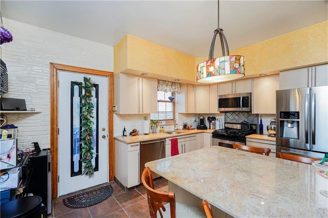 kitchen with appliances with stainless steel finishes, tasteful backsplash, a sink, dark tile patterned flooring, and light stone countertops
