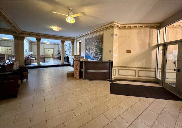 reception area with ornate columns, a ceiling fan, a decorative wall, and wainscoting