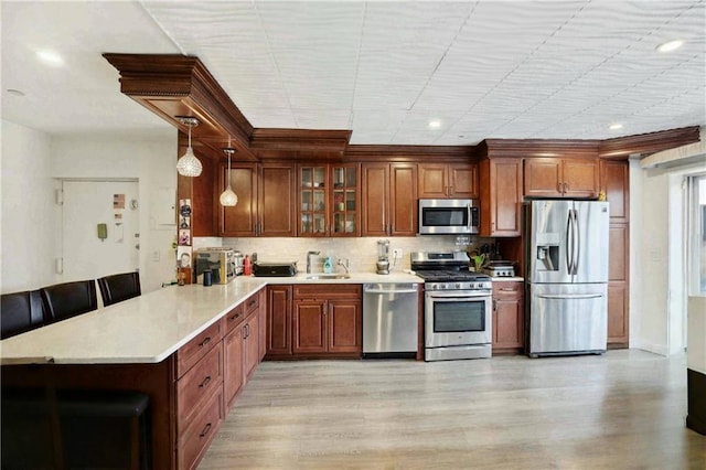 2752 Ocean Ave Unit 6A, Brooklyn, NY 11229 - kitchen featuring appliances with stainless steel finishes, a peninsula, light countertops, hanging light fixtures, and light wood-style floors