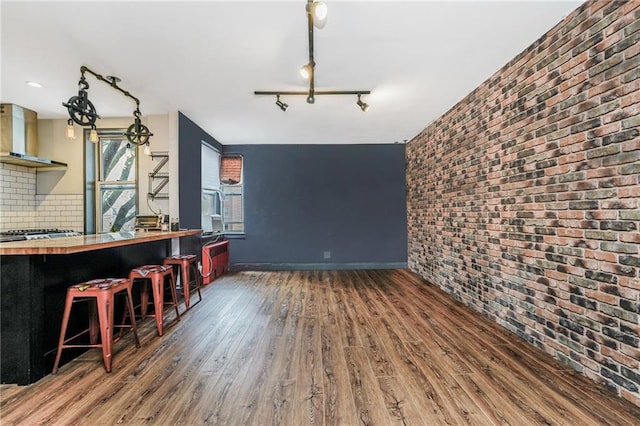 interior space with brick wall, baseboards, wood finished floors, and track lighting