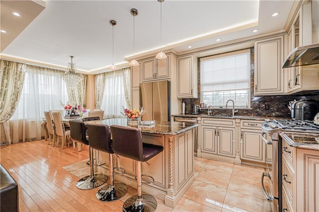 kitchen with a center island, a sink, cream cabinets, stainless steel appliances, and wall chimney exhaust hood