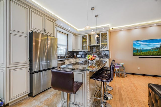 kitchen with wall chimney range hood, tasteful backsplash, a breakfast bar, cream cabinets, and stainless steel appliances