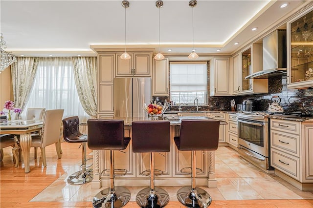 kitchen featuring decorative backsplash, cream cabinets, appliances with stainless steel finishes, and wall chimney range hood