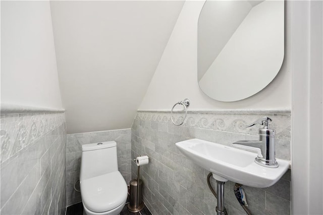 half bathroom featuring a sink, wainscoting, toilet, and tile walls