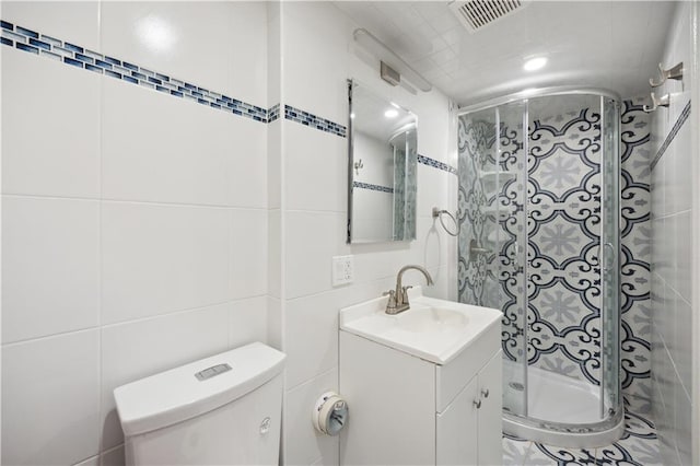 full bath with visible vents, tile walls, a stall shower, vanity, and toilet
