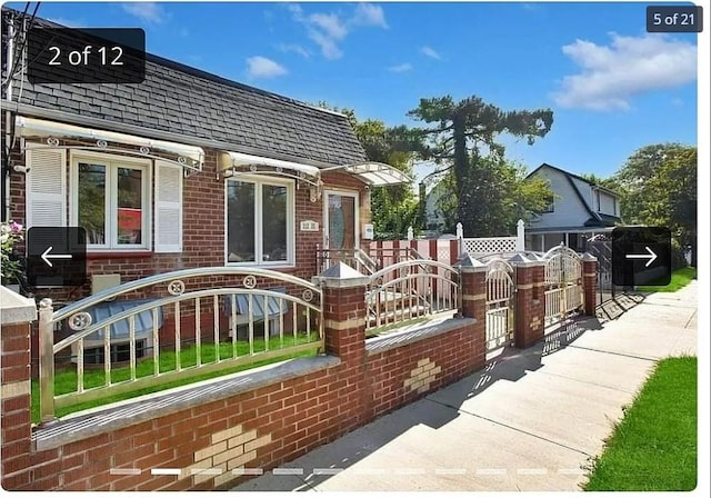 exterior space with a shingled roof, brick siding, and a fenced front yard