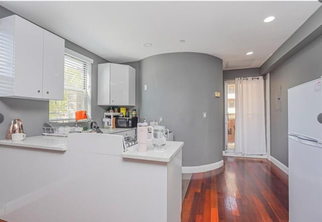 kitchen featuring freestanding refrigerator, black microwave, dark wood-type flooring, light countertops, and white cabinets