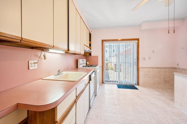 kitchen with a sink, under cabinet range hood, white appliances, light countertops, and light tile patterned floors