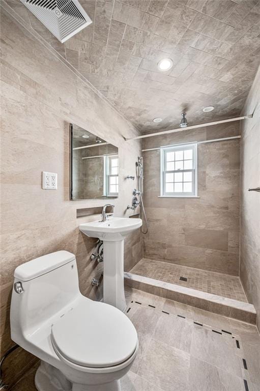bathroom with toilet, tiled shower, and tile walls