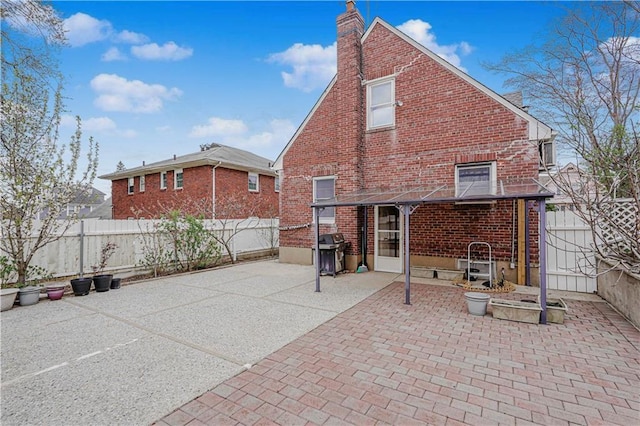 rear view of house with brick siding, a patio area, a chimney, and a fenced backyard