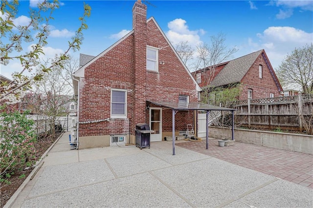 rear view of house with brick siding, a chimney, a patio area, and a fenced backyard