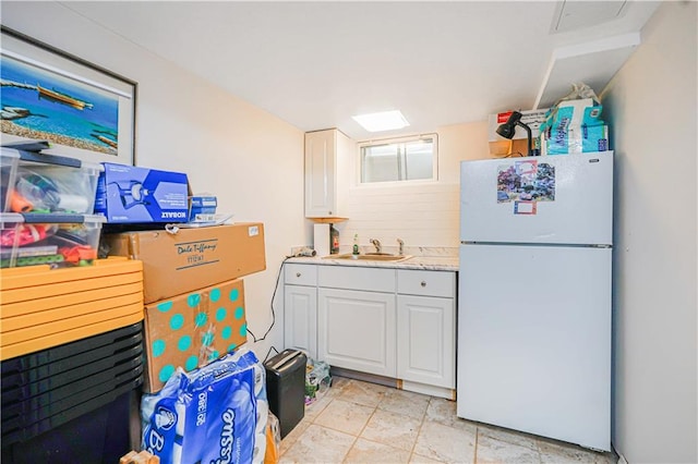 kitchen featuring freestanding refrigerator, light countertops, white cabinets, and a sink