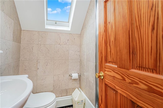 bathroom featuring a skylight, toilet, a sink, and tile walls