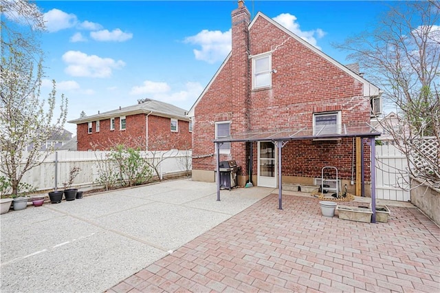 back of house with brick siding, a chimney, a patio area, and a fenced backyard