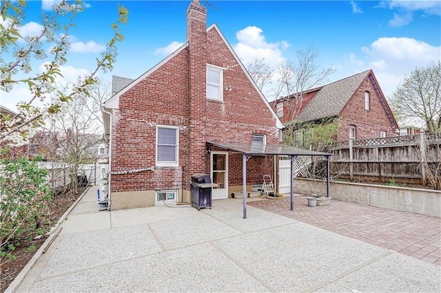 rear view of house featuring brick siding, a patio area, a chimney, and a fenced backyard