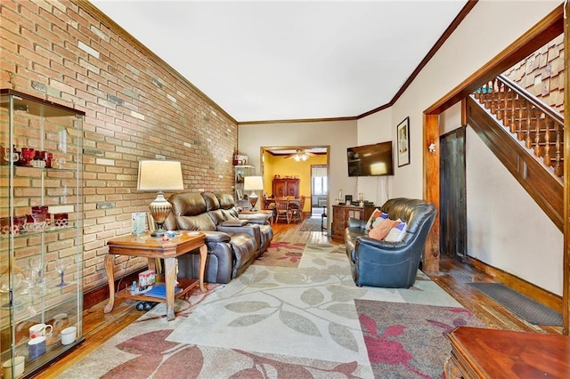 living room with wood finished floors, stairway, brick wall, crown molding, and ceiling fan