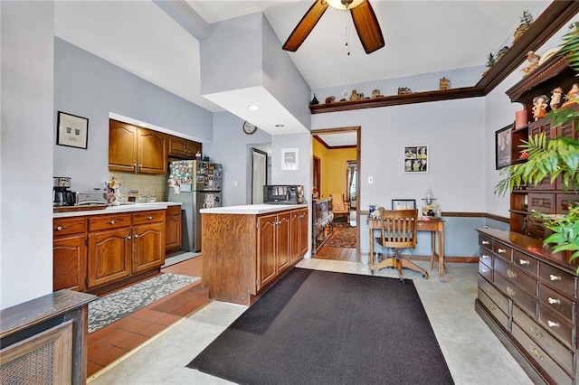 kitchen with freestanding refrigerator, a ceiling fan, tasteful backsplash, a desk, and brown cabinets